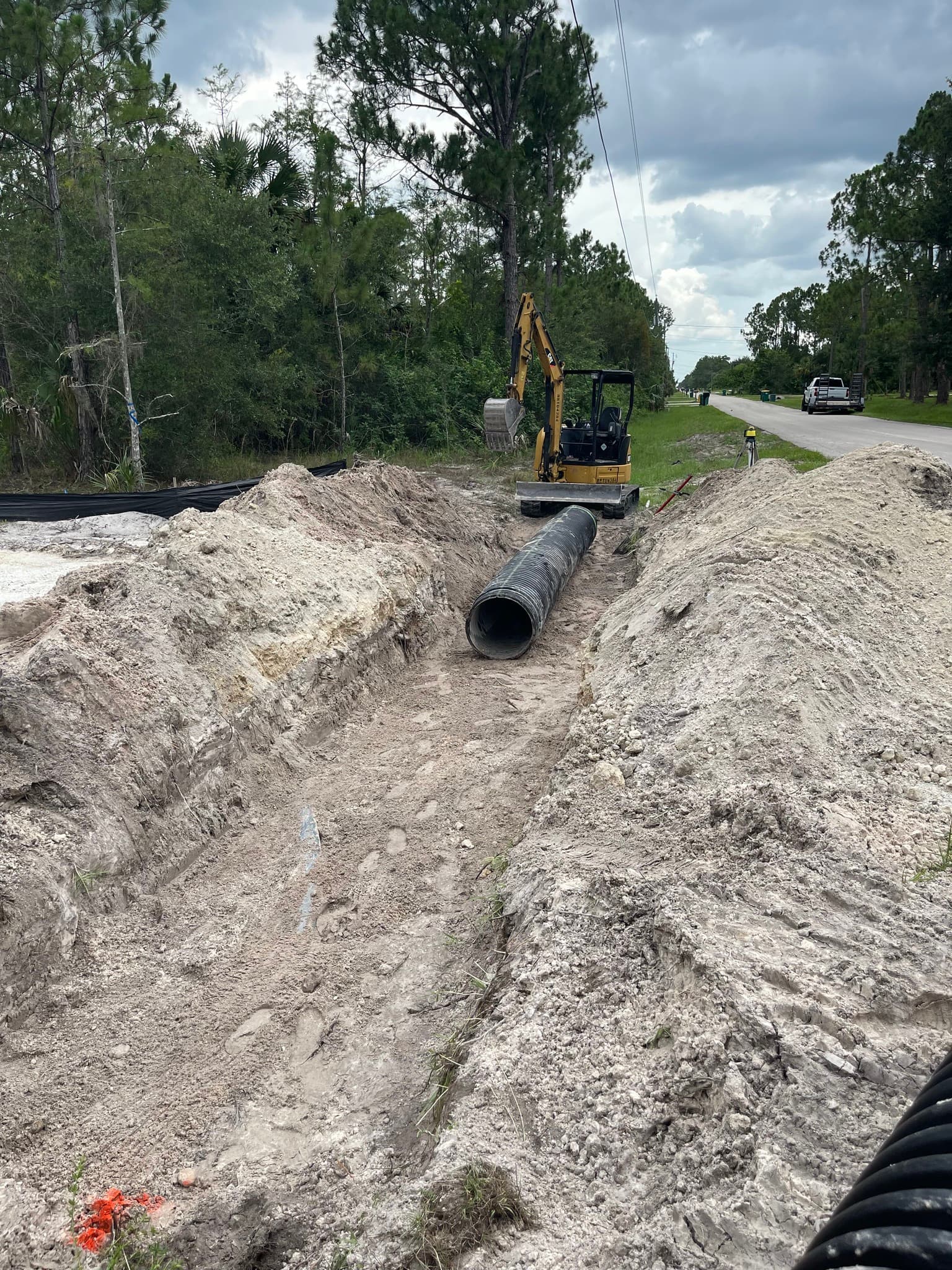 Yellow mini excavator at the end of a sandy trench with a black corrugated pipe.