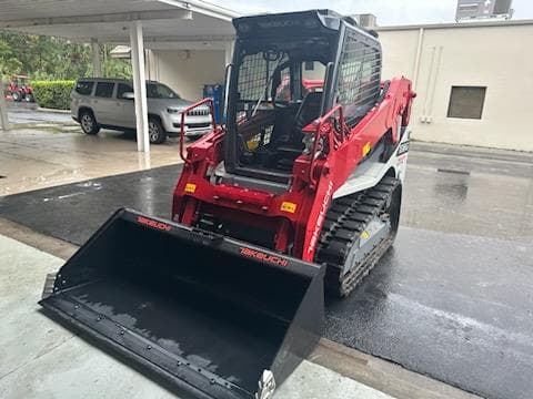 Red and white Takeuchi compact track loader with a black bucket on wet asphalt.