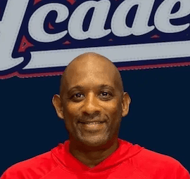 Smiling bald Black man wearing a red hoodie in front of a blue Academy logo.